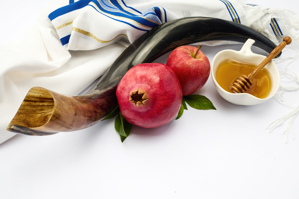 Shofar, apples, pomegranate, honey and a tallit representing Jewish New Year traditions.